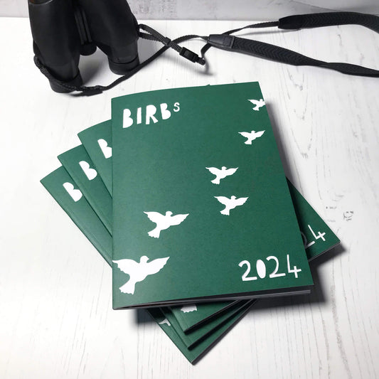 A photo of a pile of four zines by Loadofolbobbins. The cover is dark green and shows a papercut style illustration of the title which is Birbs 2025 and a series of flying bird silhouettes in a diagonal from left to right.