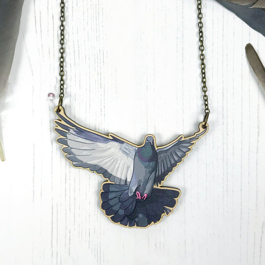 A laser cut wooden charm necklace showing an illustration of a flying pigeon with wings outstretched by loadofolbobbins. The wooden necklace is hanging from an antique bronze cable chain.