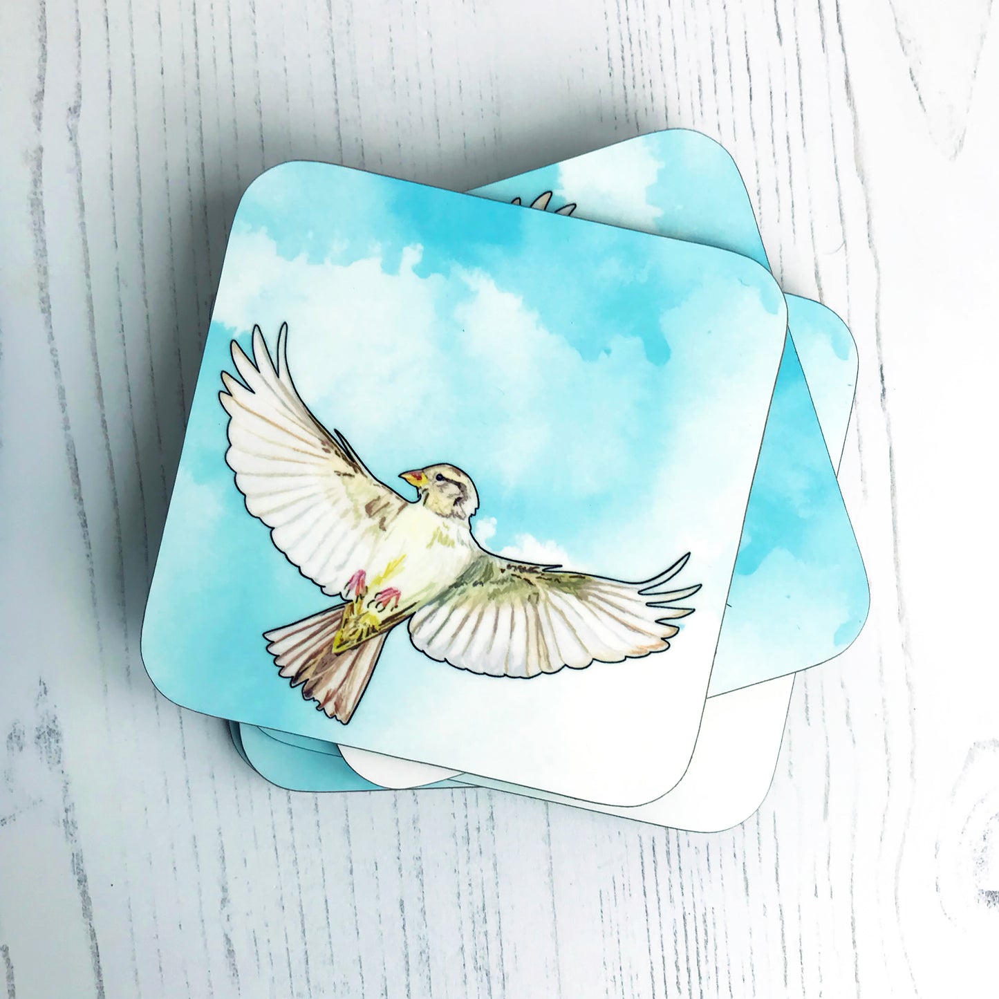 A photo of a pile of round edged square coasters which have an original illustration by Loadofolbobbins showing a flying female sparrow with wings spread out. The background is an inky wash in bright turquoise.