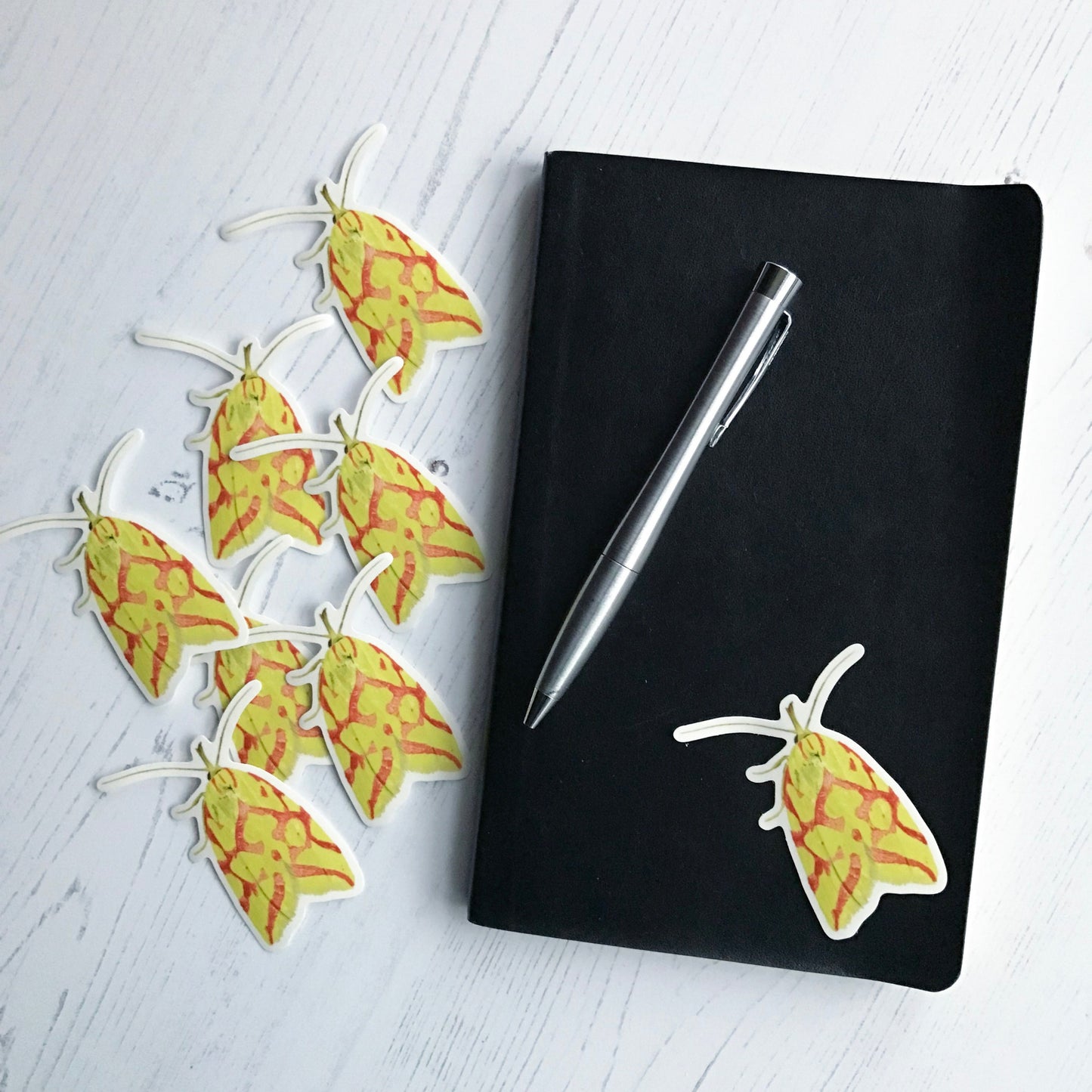 A hypercallia citrinilis moth sticker created from an original digital illustration by Loadofolbobbins. The moth has it's wings closed behind it and looks to the viewer as if it has just perched on a surface vertically in front of them. The moth itself is a bright almost neon yellow with a network of connected patches and irregular lines in a red almost coral colour. The long thin antennae and legs are also yellow as well an almost trunk like extension from it's head that curves upwards.
