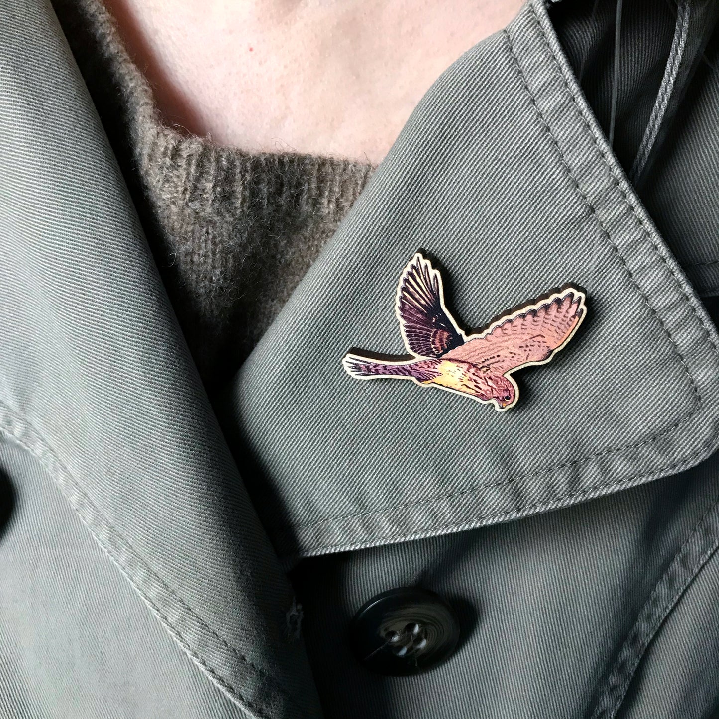 A laser cut wooden brooch showing an illustration by Loadofolbobbins of a flying pigeon with wings spread out wide. The brooch is worn on the lapel of a jacket.