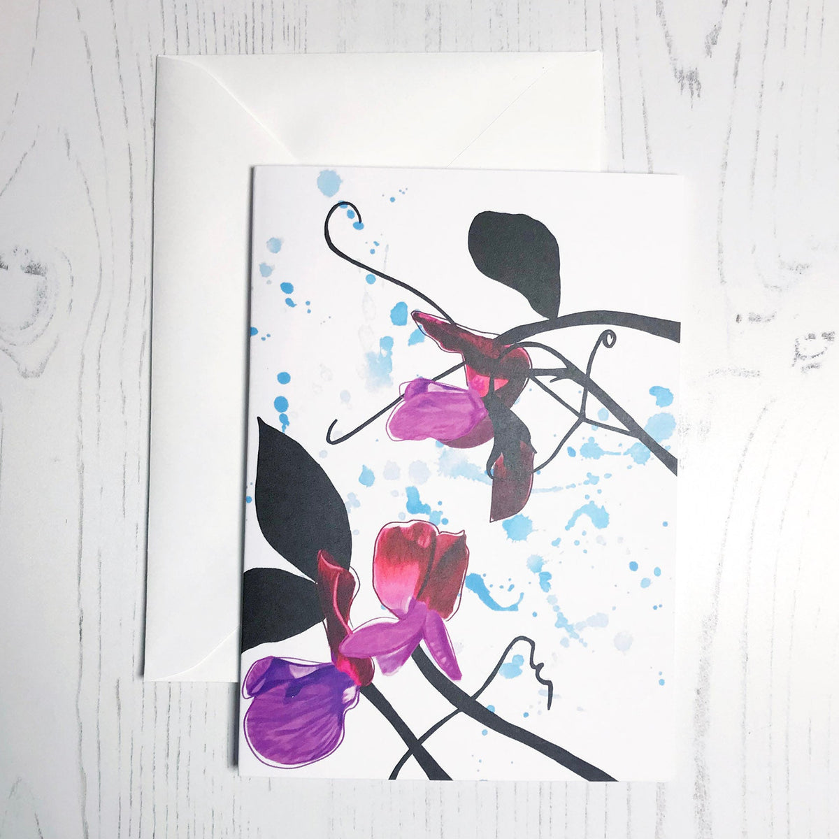 An A6 greetings card showing an illustration of sweet peas against an inky blue wash background. The purple sweet peas flowers are in colour with the plant leaves and stems silhouetted in black.
