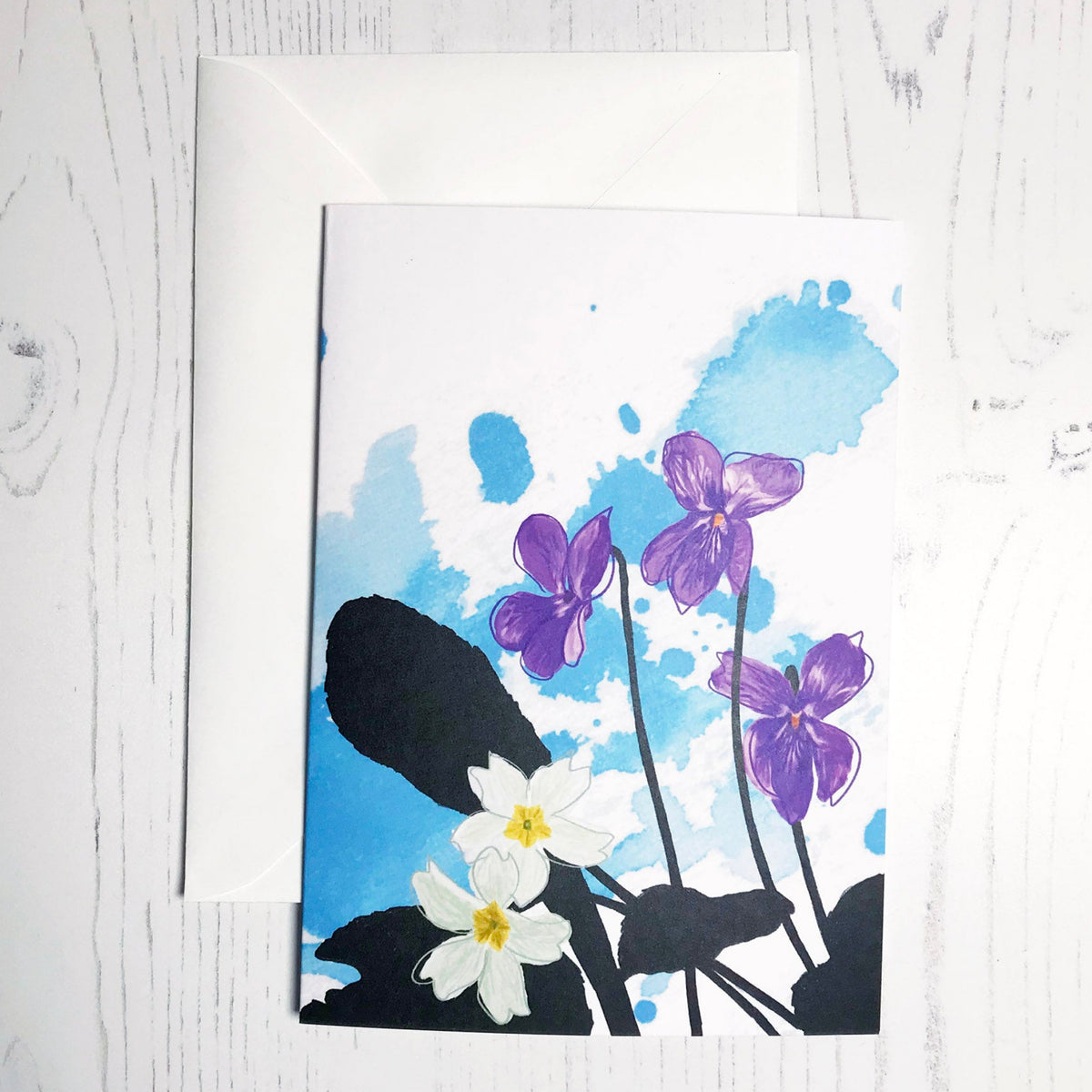 An A6 greetings card showing an illustration of a violets and evening primroses against an inky blue wash background. The violet and primrose flowers are in colour with the plant leaves silhouetted in black.