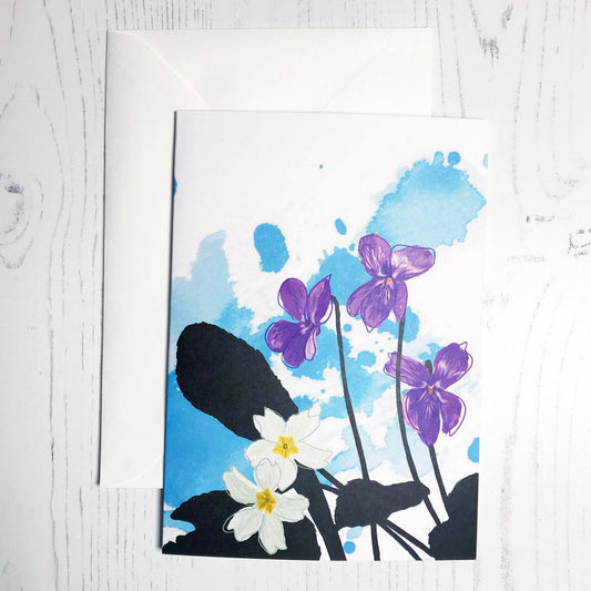An A6 greetings card showing an illustration of a violets and evening primroses against an inky blue wash background. The violet and primrose flowers are in colour with the plant leaves silhouetted in black.
