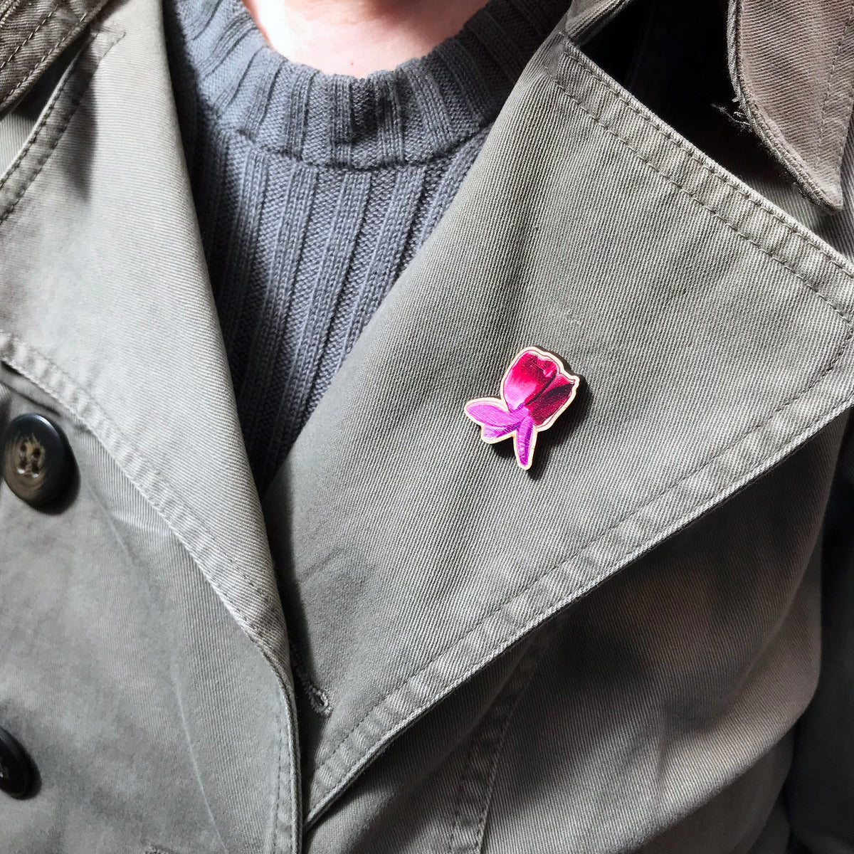 A 25mm mini wooden lapel pin of a pinky purple sweet pea flower worn on the lapel of a jacket. The pin is made from an original illustration and is loose and expressive in style. 