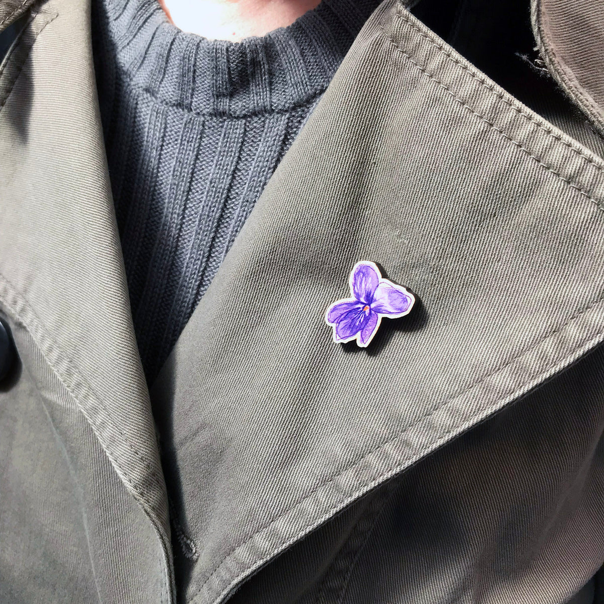 A 25mm mini wooden lapel pin of a purple violet flower worn on the lapel of a jacket. The pin is made from an original illustration and is loose and expressive in style. 