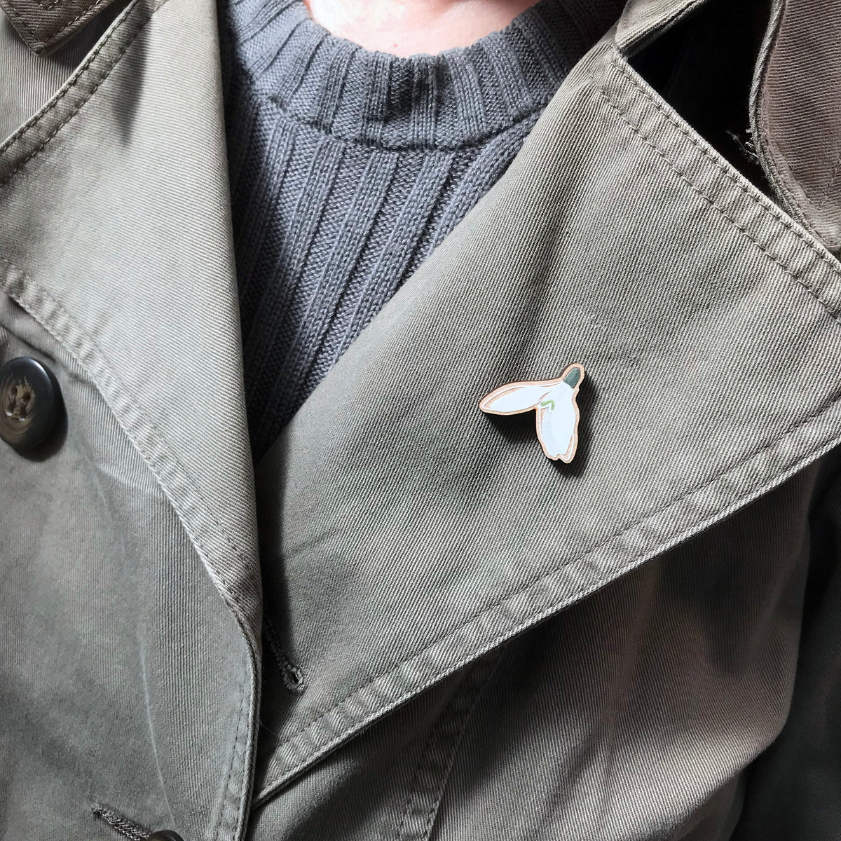 A 25mm mini wooden lapel pin of a snowdrop flower worn on the lapel of a jacket. The pin is made from an original illustration and is loose and expressive in style. 