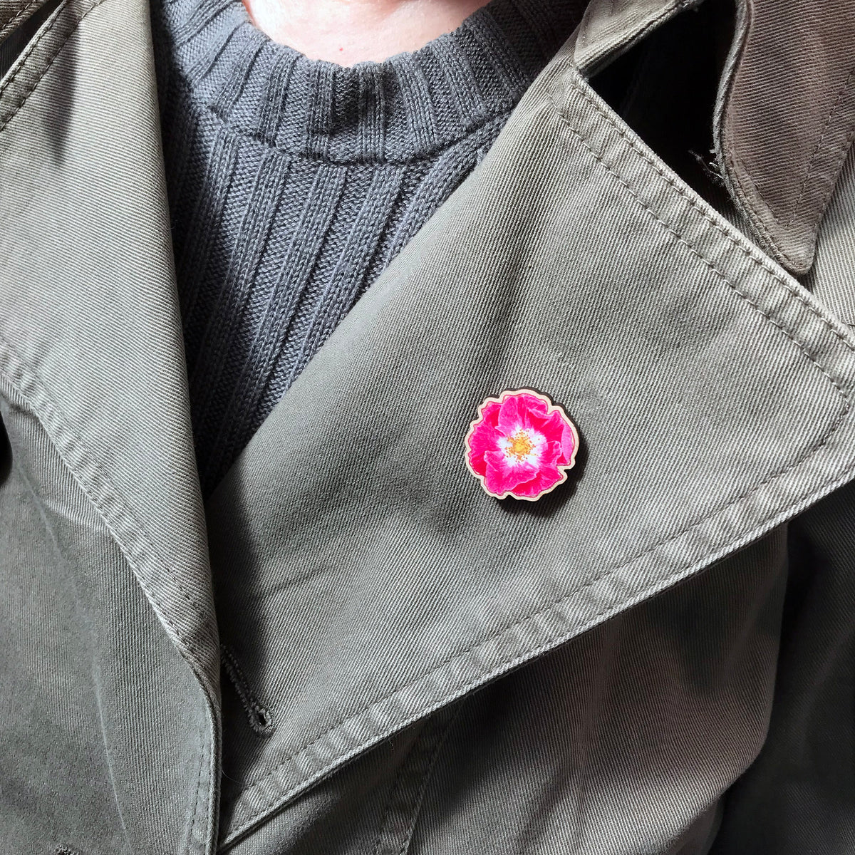 A 25mm mini wooden lapel pin of a pink dog rose flower worn on the lapel of a jacket. The pin is made from an original illustration and is loose and expressive in style. 