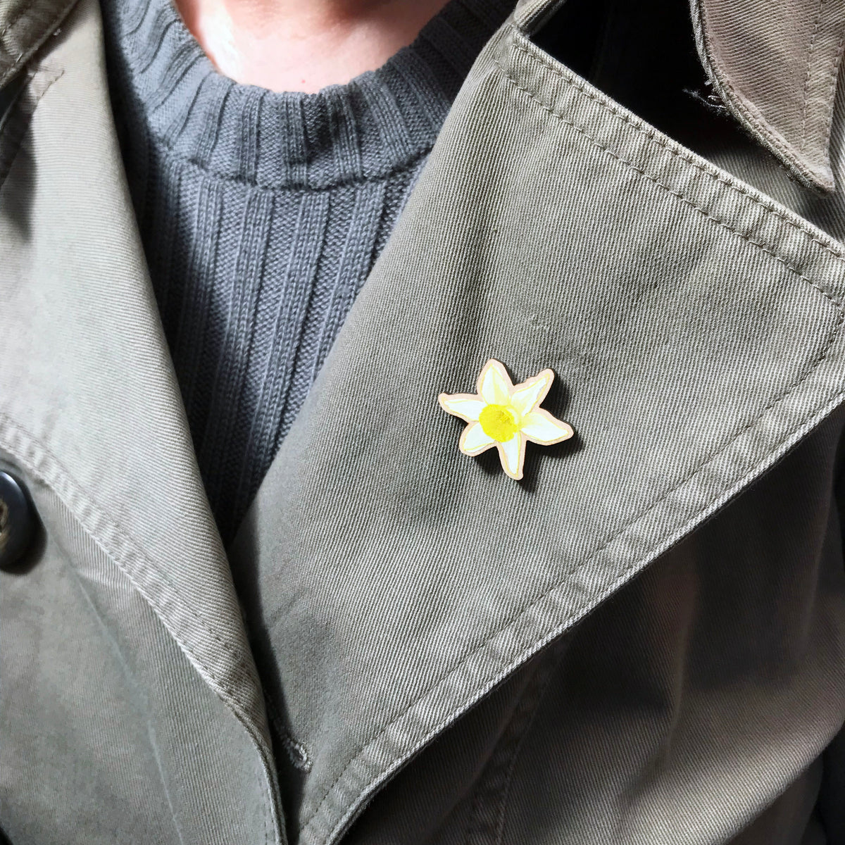 A 25mm mini wooden lapel pin of a yellow daffodil flower worn on the lapel of a jacket. The pin is made from an original illustration and is loose and expressive in style. 