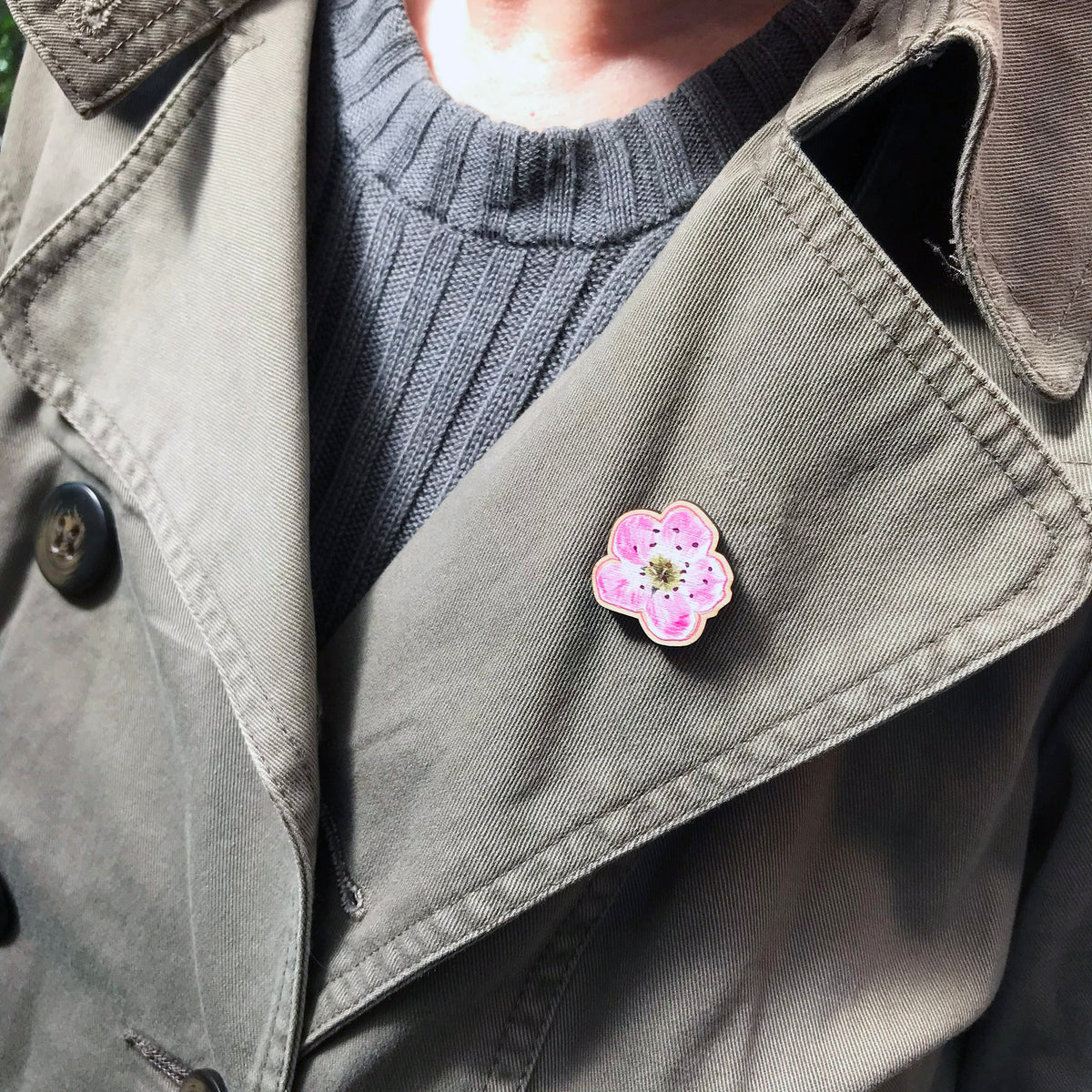 A 25mm mini wooden lapel pin of a pinky white hawthorn blossom worn on the lapel of a jacket. The pin is made from an original illustration and is loose and expressive in style. 