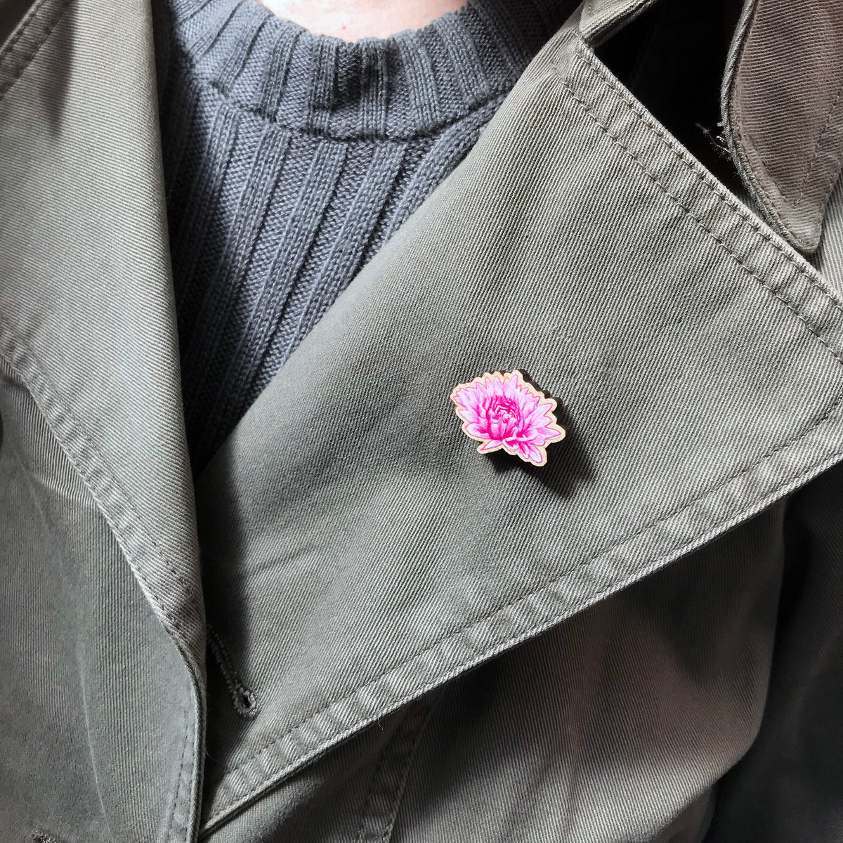 A 25mm mini wooden lapel pin of a pink chrysanthemum flower worn on the lapel of a jacket. The pin is made from an original illustration and is loose and expressive in style. 