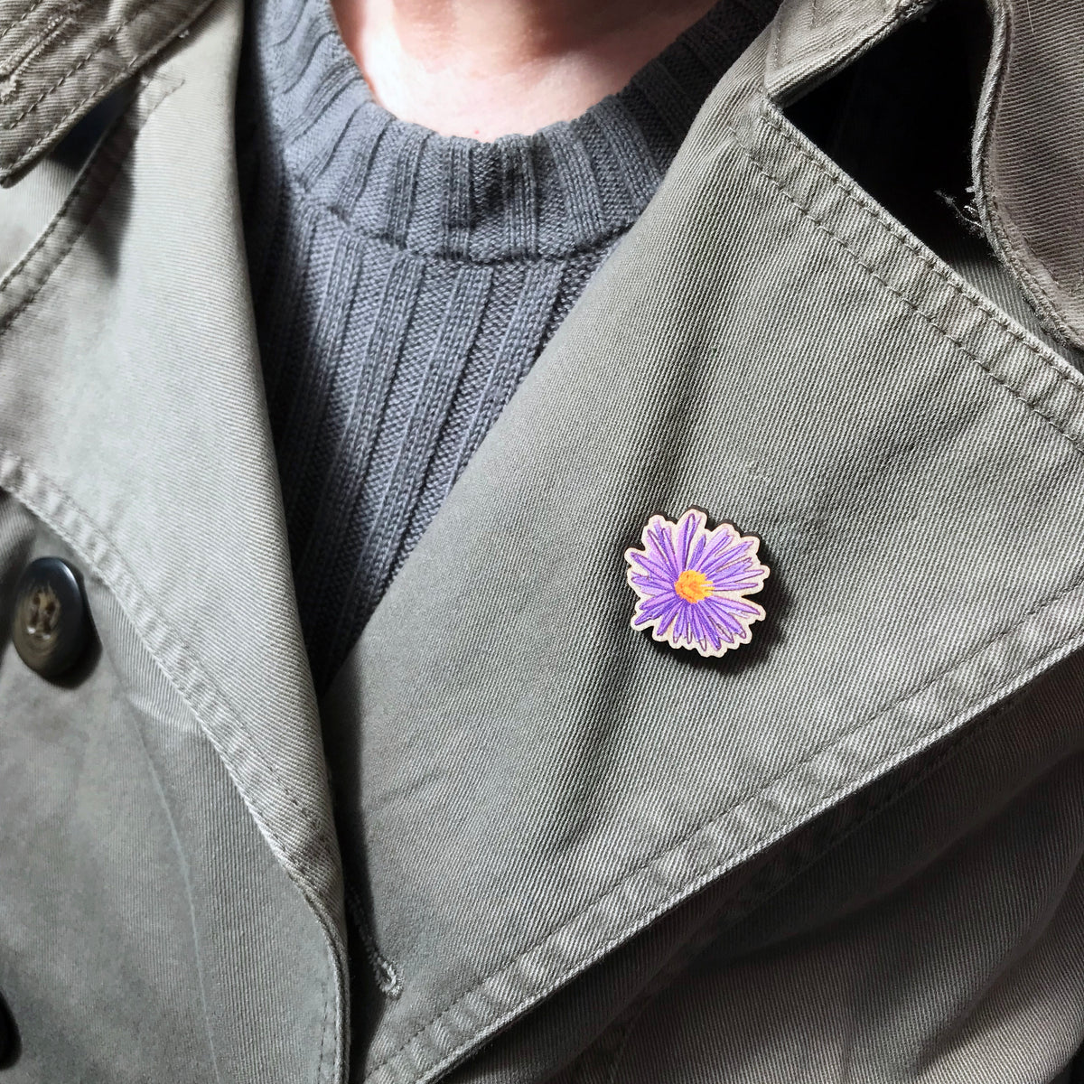 A 25mm mini wooden lapel pin of a purple aster flower worn on the lapel of a jacket. The pin is made from an original illustration and is loose and expressive in style. 