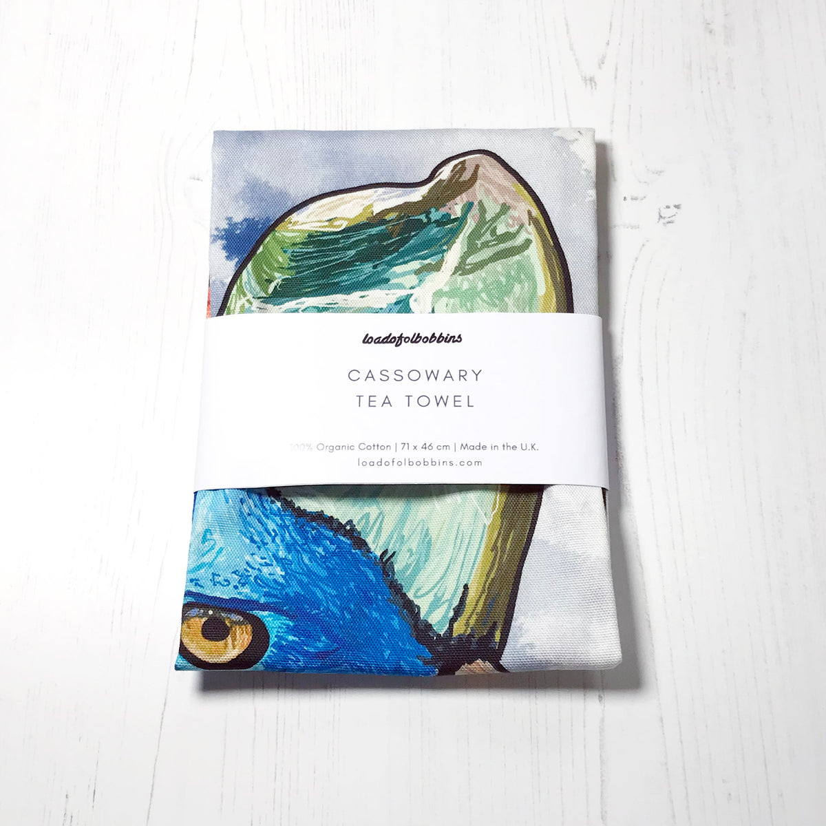 A folded bird themed illustration tea towel by loadofolbobbins. It shows the head of a Cassowary against an inky wash dark blue and white background.