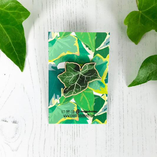 A laser cut wooden brooch showing an illustration by Loadofolbobbins of a dark green ivy leaf. The brooch is mounted on a backing card with a repeat ivy leaf pattern.