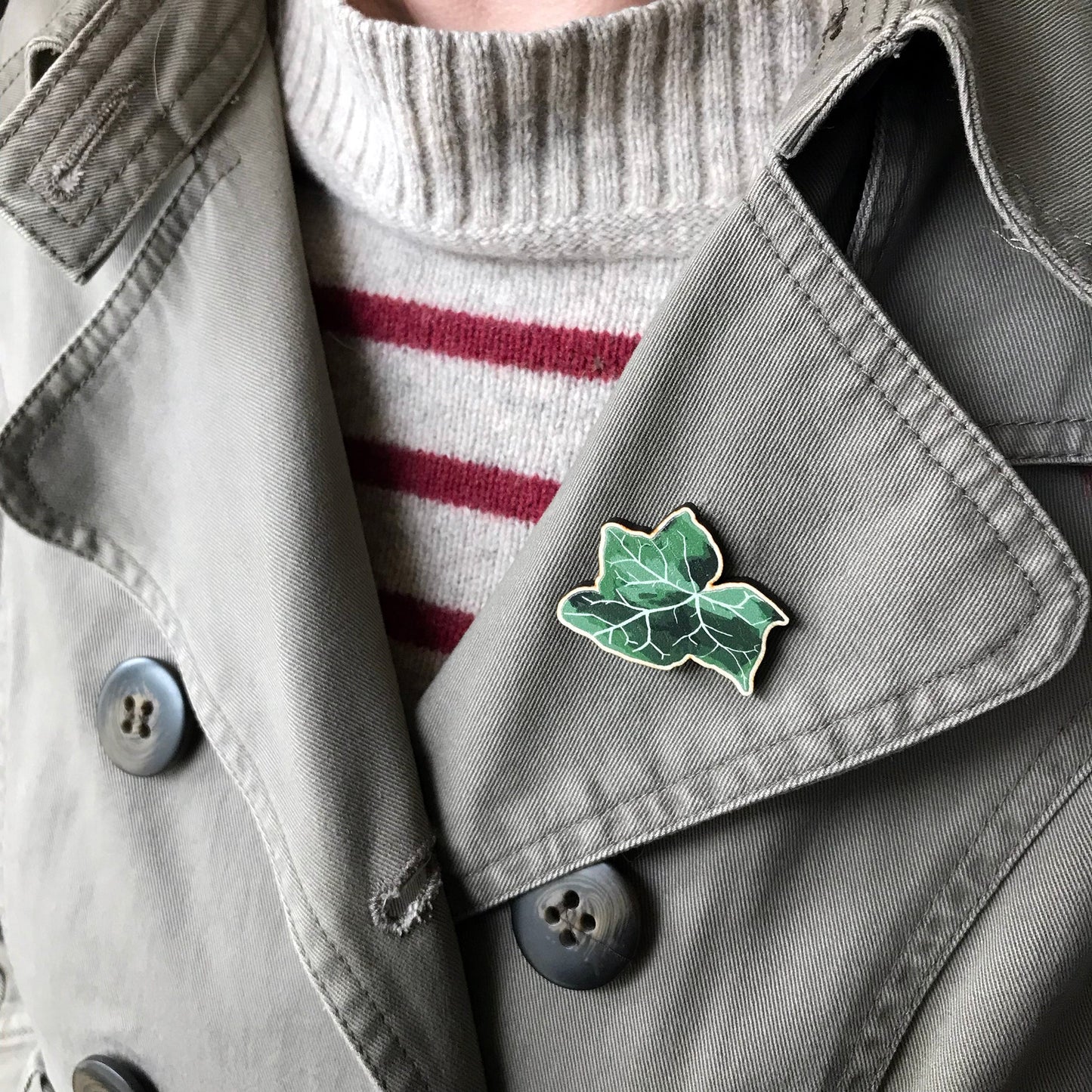 A laser cut wooden brooch showing an illustration by Loadofolbobbins of an ivy leaf. The brooch is worn on the lapel of a jacket.