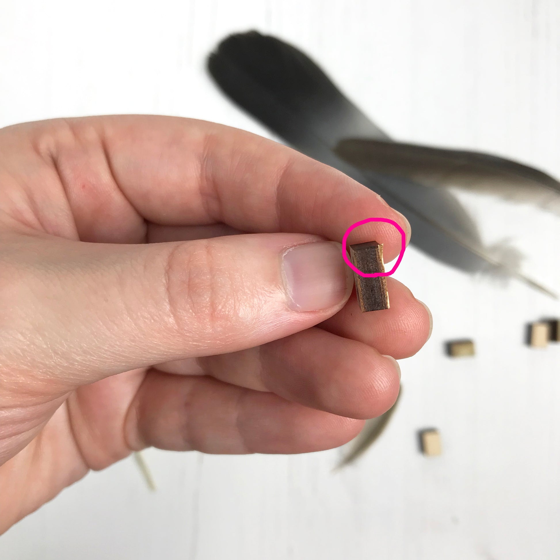 A laser cut wooden stud earring second by loadofolbobbins showing a silhouette scene inspired by the novel Jane Eyre by Charlotte Brontë. The stud is side on and a pink circle is highlighting where the edge is slightly chipped.