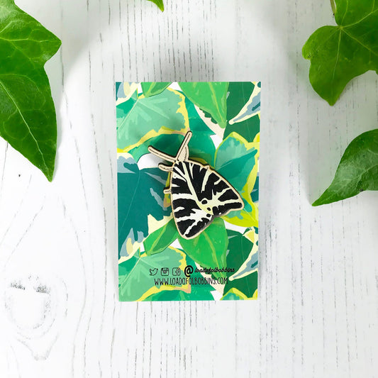 A laser cut wooden brooch showing an illustration by Loadofolbobbins of a Jersey Tiger moth. The brooch is mounted on a backing card with a repeat ivy leaf pattern.
