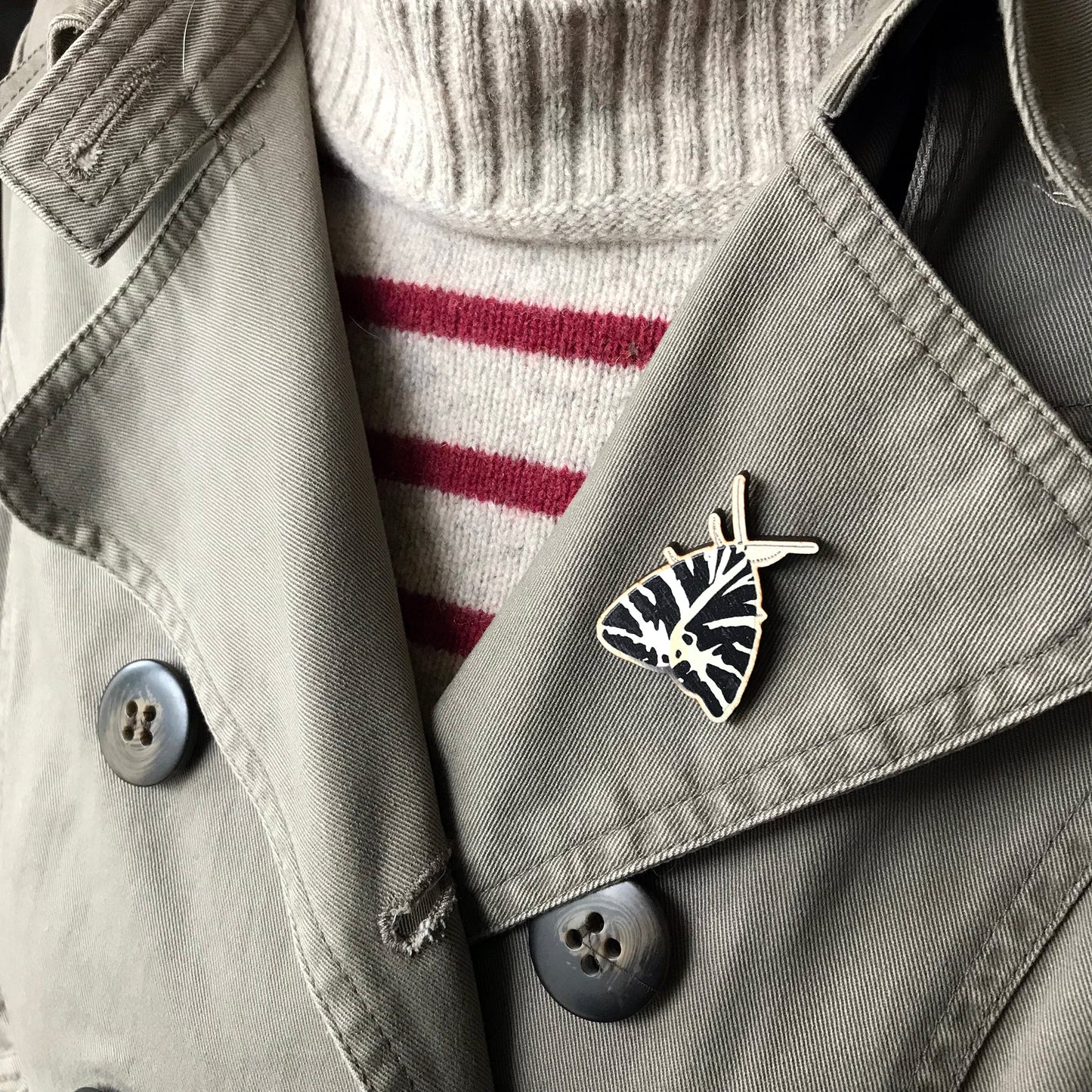 A laser cut wooden brooch showing an illustration by Loadofolbobbins of a Jersey Tiger Moth. The brooch is worn on the lapel of a jacket.