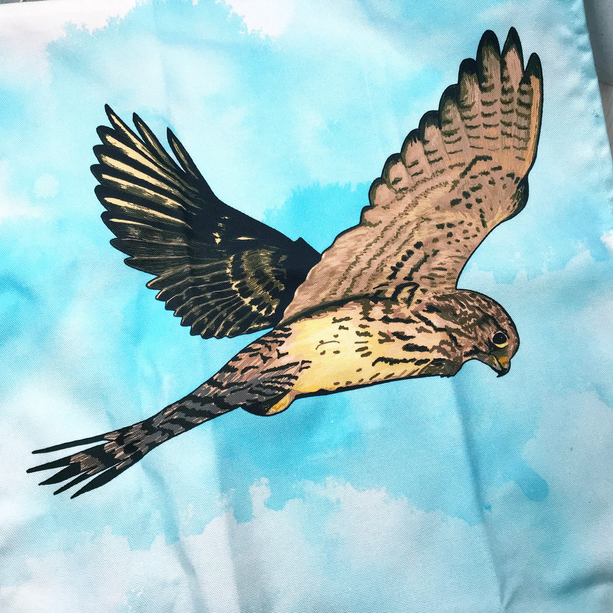 A close up photo of a tea towel showing an illustration of a hovering kestrel against an inky wash turquoise and white background.