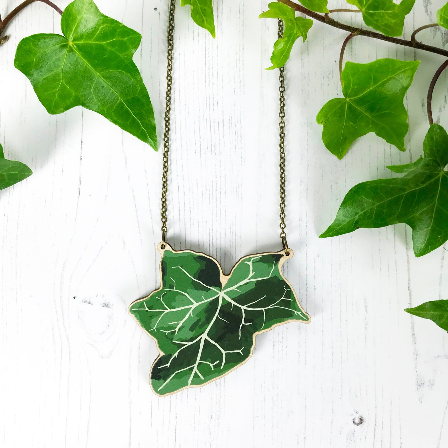 A laser cut wooden statement necklace showing an illustration of an dark green ivy leaf by loadofolbobbins. The wooden necklace is hanging from an antique bronze cable chain.