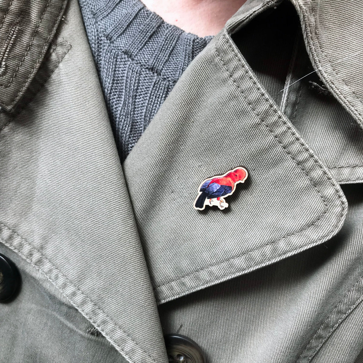 A 30mm mini wooden lapel pin of a Andean cock-of-the-rock bird perched on a branch and worn on the lapel of a jacket. The pin is made from an original illustration and is detailed and expressive in style. The bird is orange and black with a distinct circular crest on it's head.