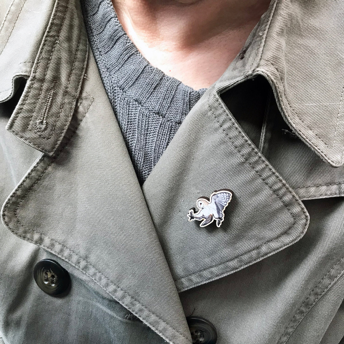 A 30mm mini wooden lapel pin of a swooping barn owl worn on the lapel of a jacket. The pin is made from an original illustration and is detailed and expressive in style. The bird is creams and browns with wings in full flight. 