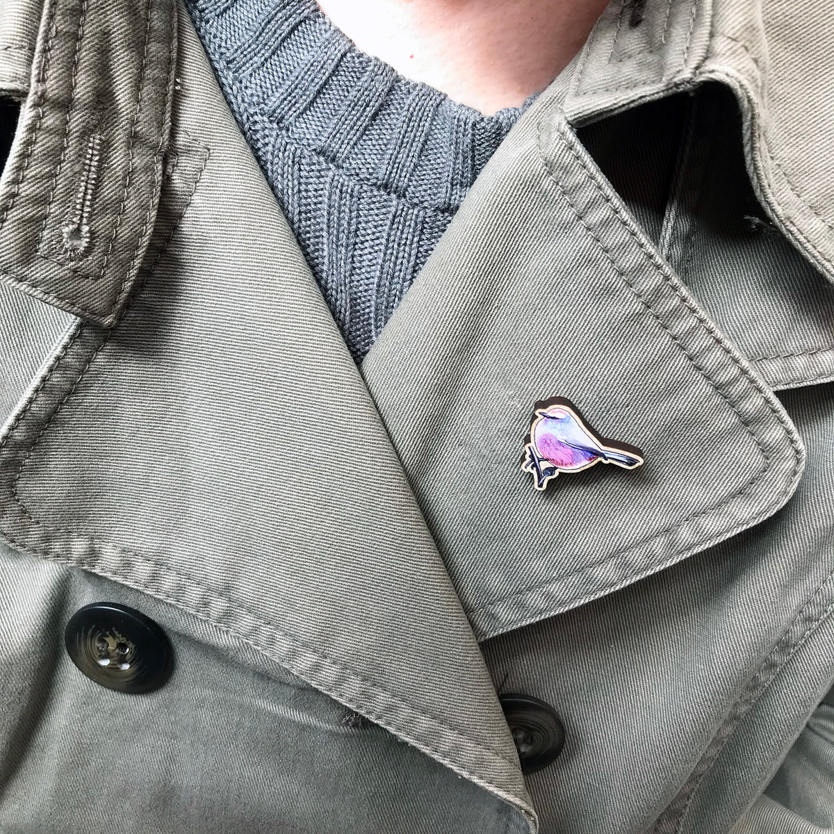 A 26mm mini wooden lapel pin of a white-browed tit warbler worn on the lapel of a jacket. The pin is made from an original illustration and is detailed and expressive in style. The bird is a mix of amazing pinks, purples and blues. 