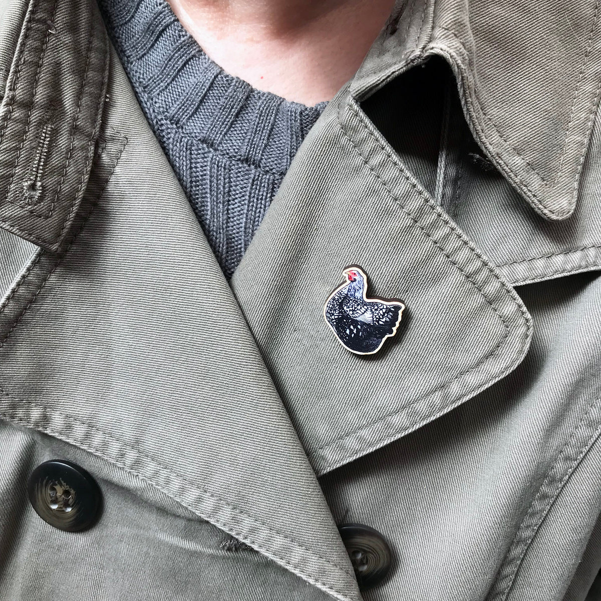 A 26mm mini wooden lapel pin of a Wyandotte chicken worn on the lapel of a jacket. The pin is made from an original illustration and is detailed and expressive in style. The bird is has a lacy black and white pattern. 
