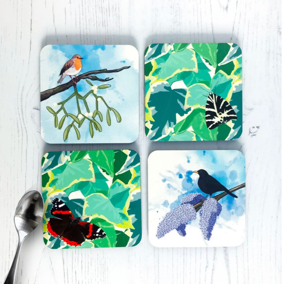 A series of four colourful nature themed coasters created from illustrations by Loadofolbobbins. Clockwise from top left they show a robin perching on a branch with mistletoe hanging from it, a Jersey tiger Moth perched on a background of ivy, a male blackbird perched on a branch of blooming lilac with an inky blue wash background and a red admiral butterfly perching on a ivy leaf background.