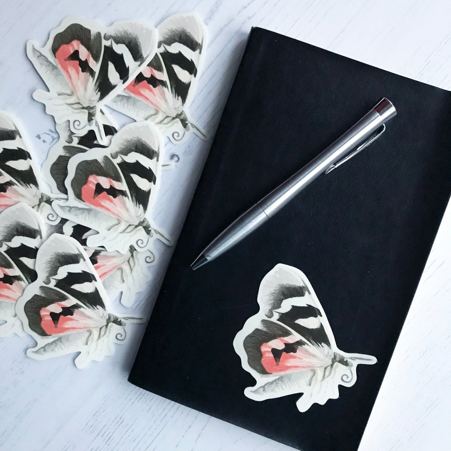 A red underwing moth sticker created from an original digital illustration by Loadofolbobbins. A large moth, it's side on to the viewer with wings back flapping in mid flight. It's wings have a cream colour which is broken up by thick bold black striped patches and on the lower wing a section of red colouring. The body of the moth is segmented and is cream in colour with grey brown speckled markings running down the centre. It's head is grey brown with similarly coloured antennae and it's curled proboscis.