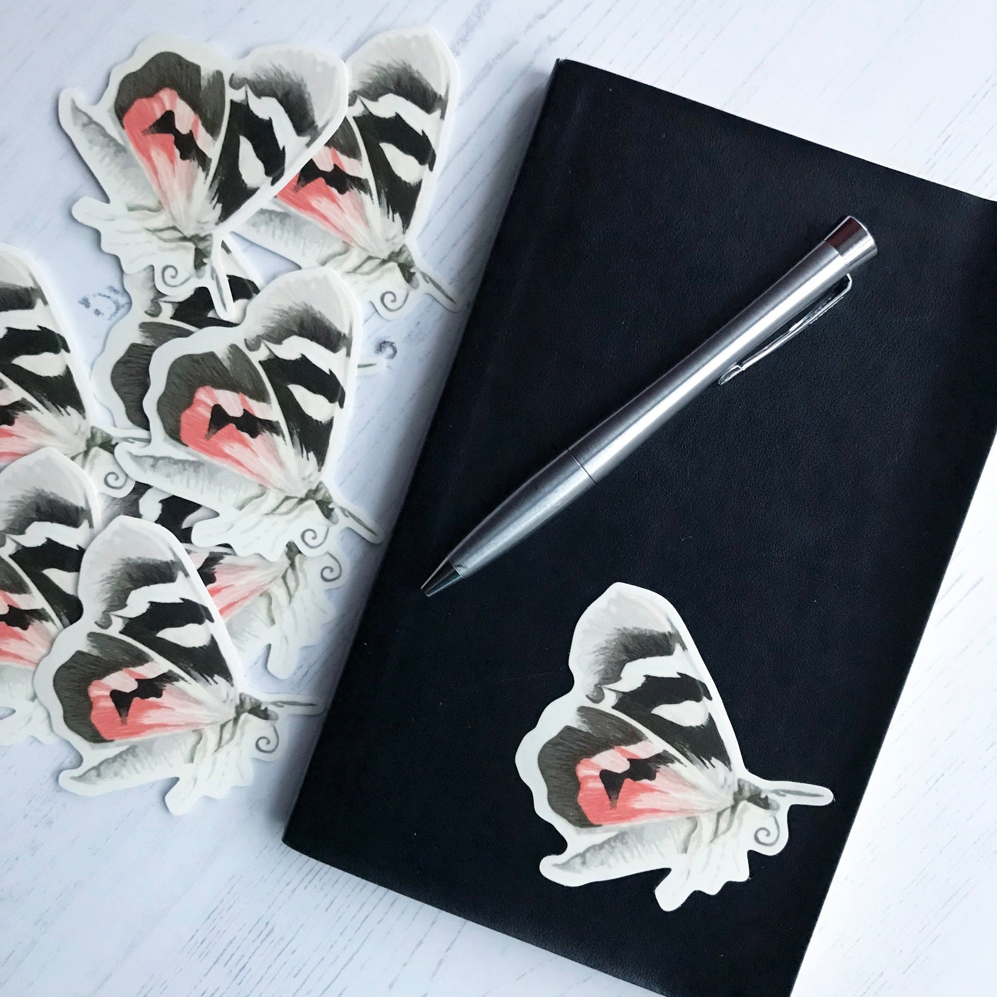 A red underwing moth sticker created from an original digital illustration by Loadofolbobbins. A large moth, it's side on to the viewer with wings back flapping in mid flight. It's wings have a cream colour which is broken up by thick bold black striped patches and on the lower wing a section of red colouring. The body of the moth is segmented and is cream in colour with grey brown speckled markings running down the centre. It's head is grey brown with similarly coloured antennae and it's curled proboscis.