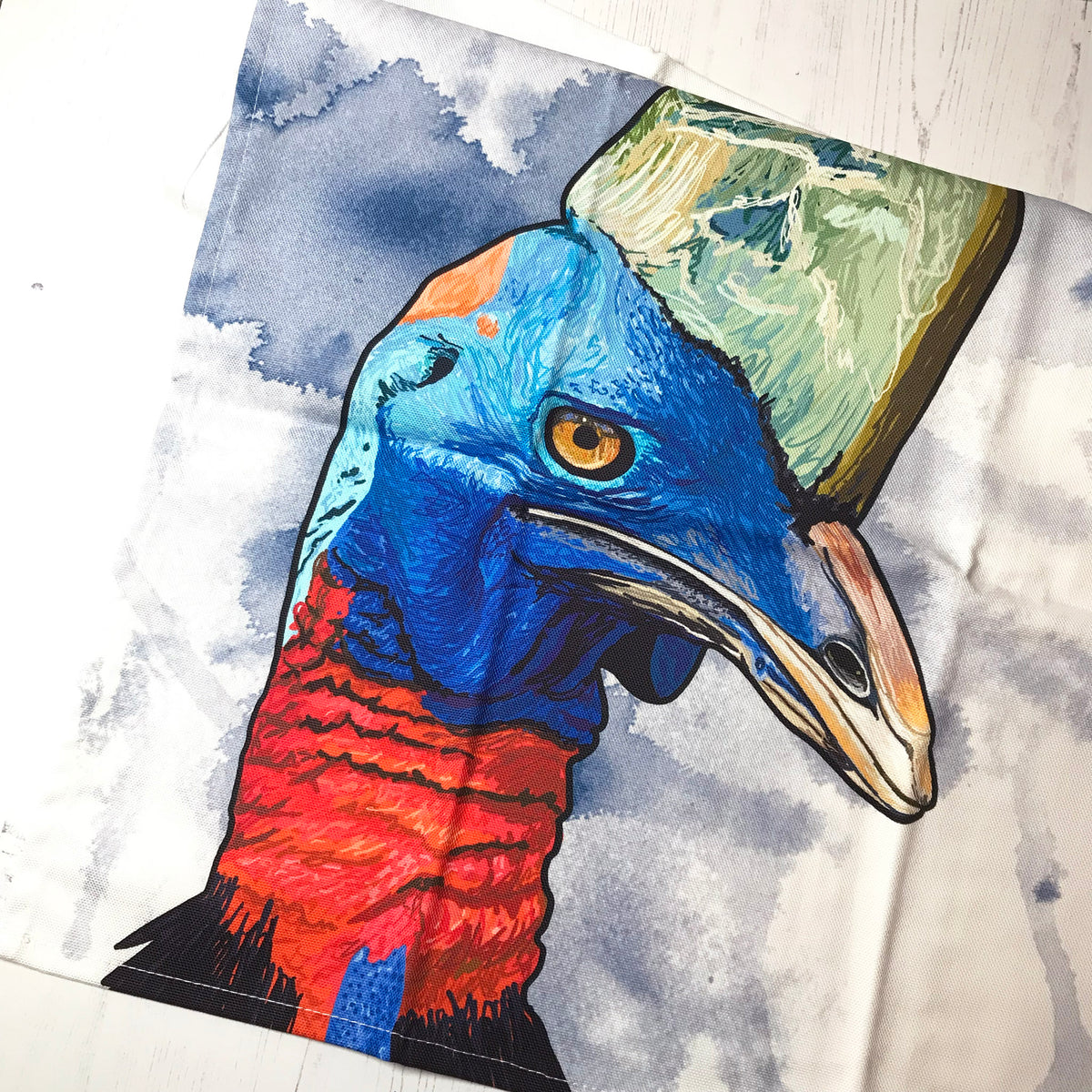A close up photo of a tea towel showing an illustration of a the head of a cassowary bird against an inky wash background.