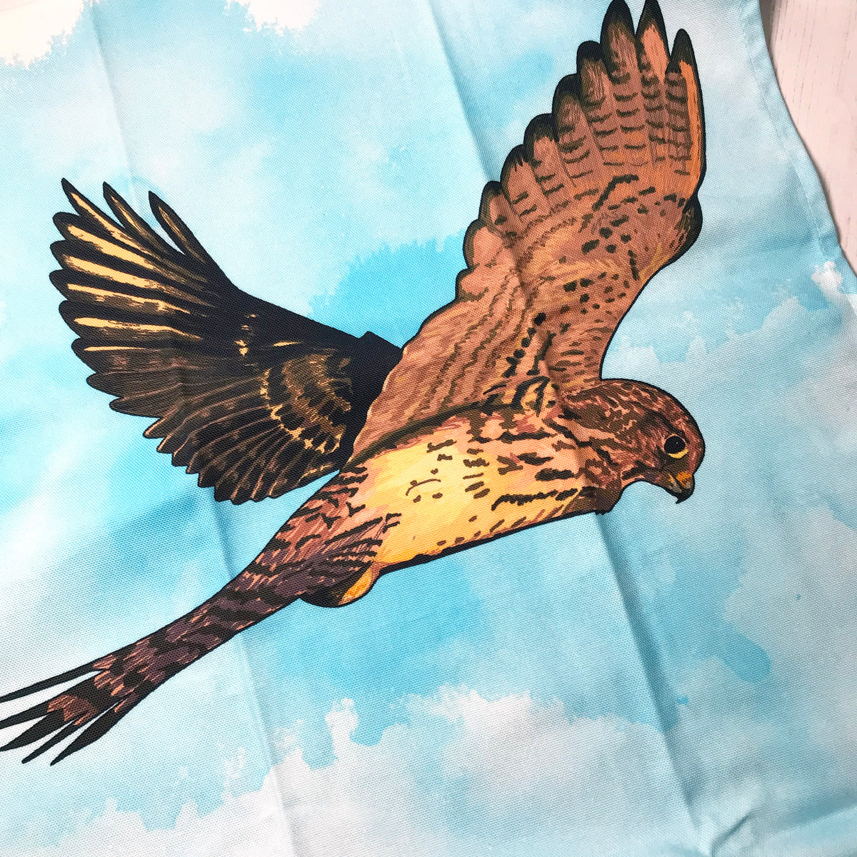 A close up photo of a tea towel showing an illustration of a hovering kestrel against an inky wash background.