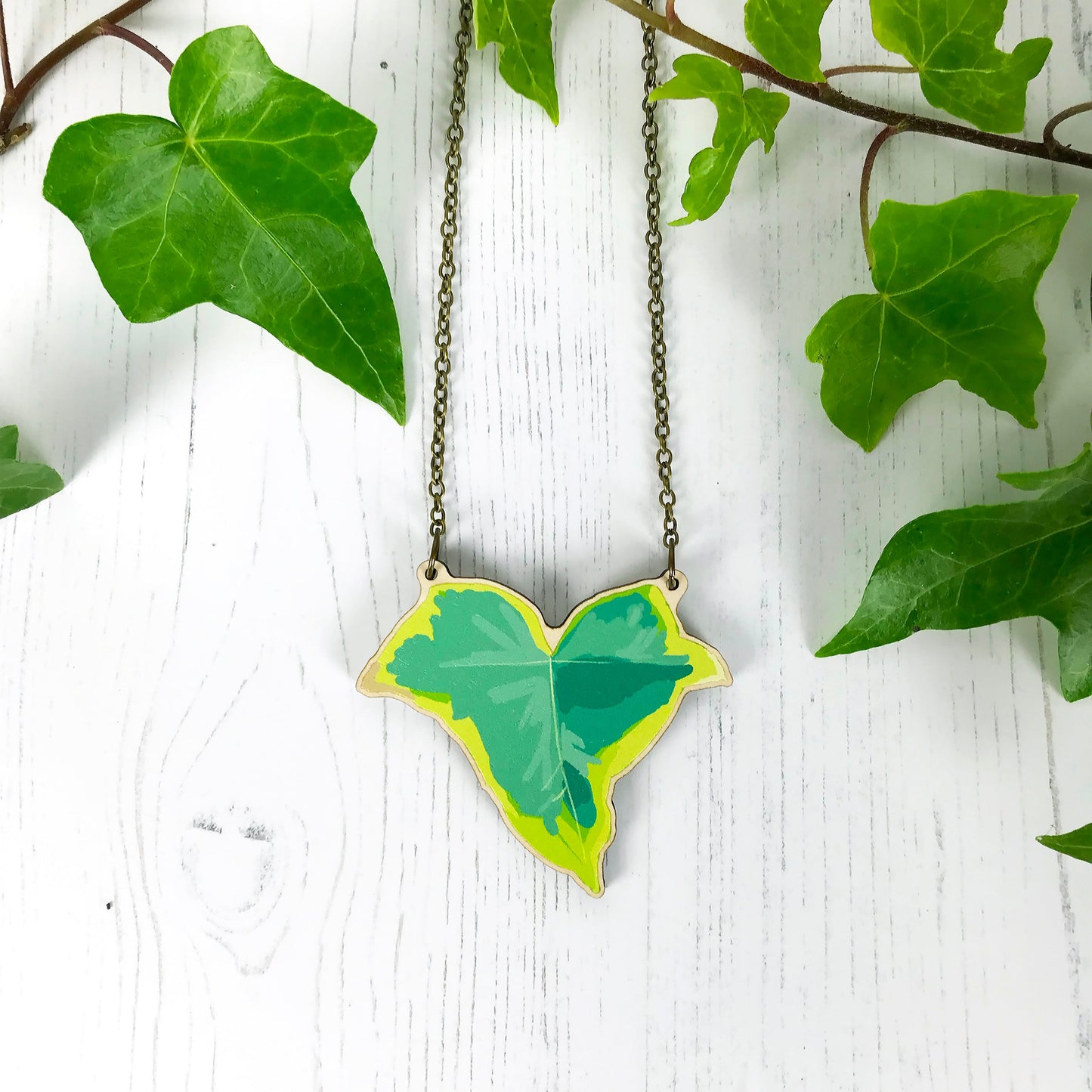 A laser cut wooden statement necklace showing an illustration of an variegated ivy leaf  by loadofolbobbins. The wooden necklace is hanging from an antique bronze cable chain.