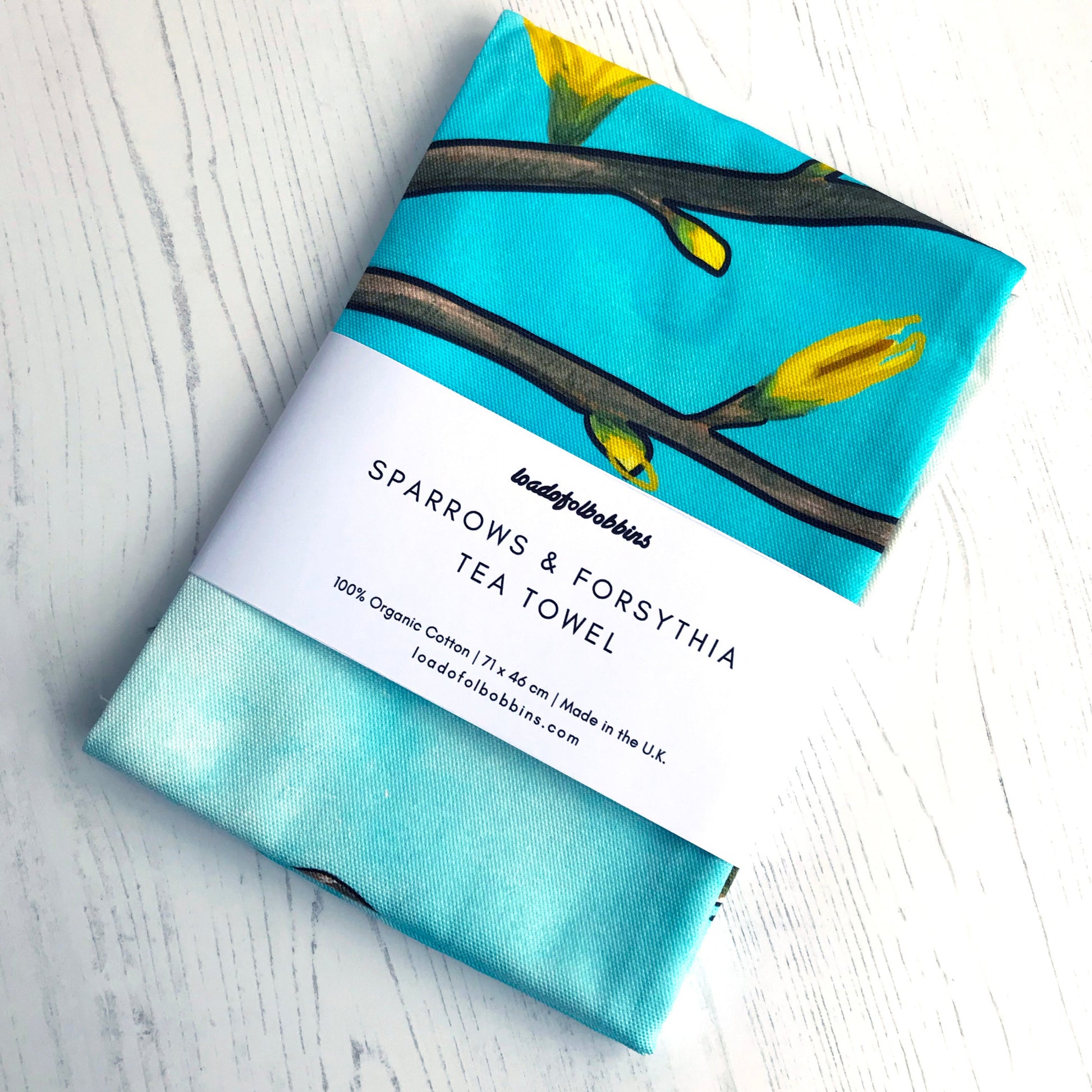 Text on belly band around a folded teatowel says. Sparrow and Forsythia tea towel. 100% organic cotton, 71 x 41 cm, made in the UK, loadofolbobbins.com