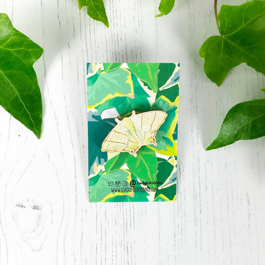 A laser cut wooden brooch showing an illustration by Loadofolbobbins of a swallowtail moth. The brooch is mounted on a backing card with a repeat ivy leaf pattern.