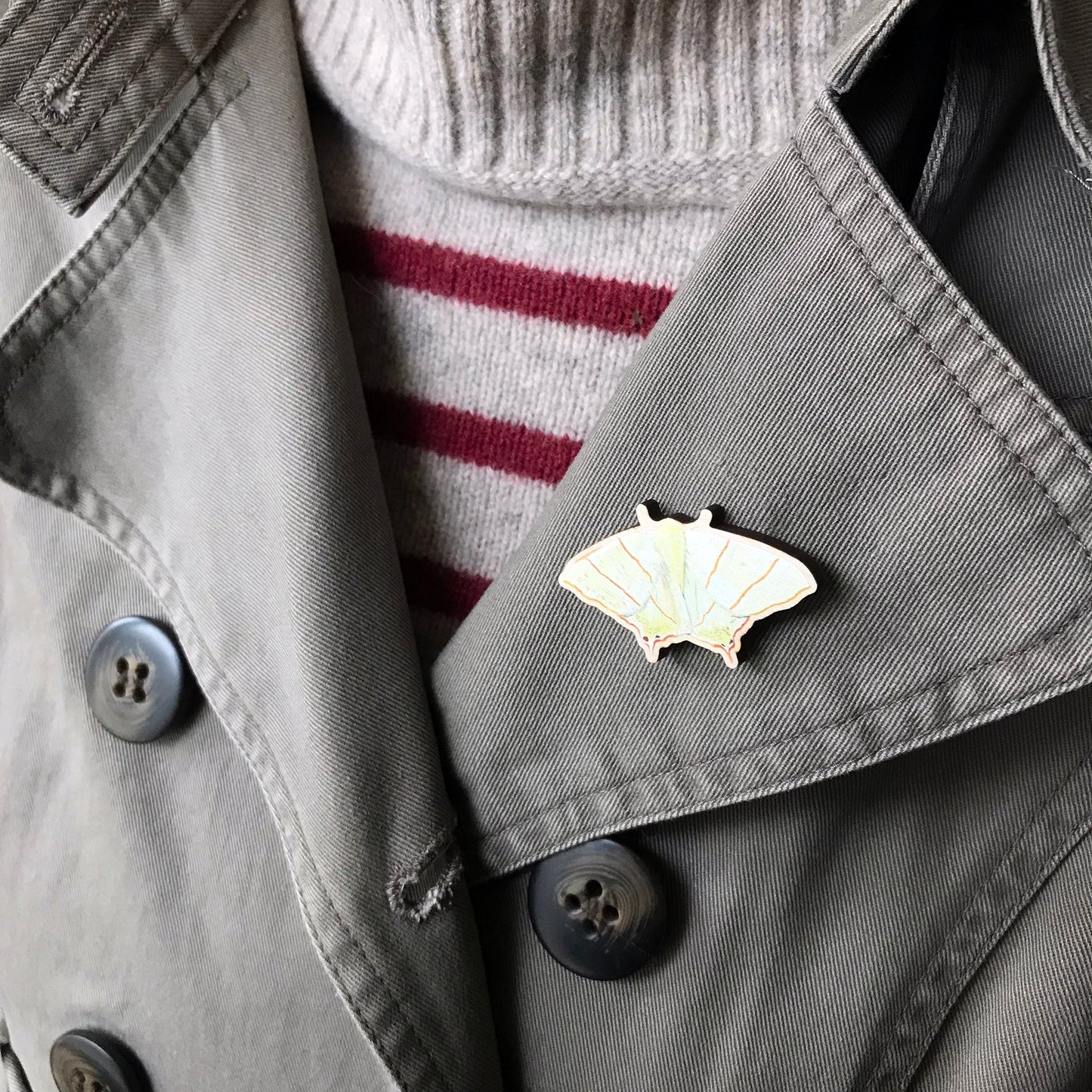 A laser cut wooden brooch showing an illustration by Loadofolbobbins of a Swallowtail Moth. The brooch is worn on the lapel of a jacket.