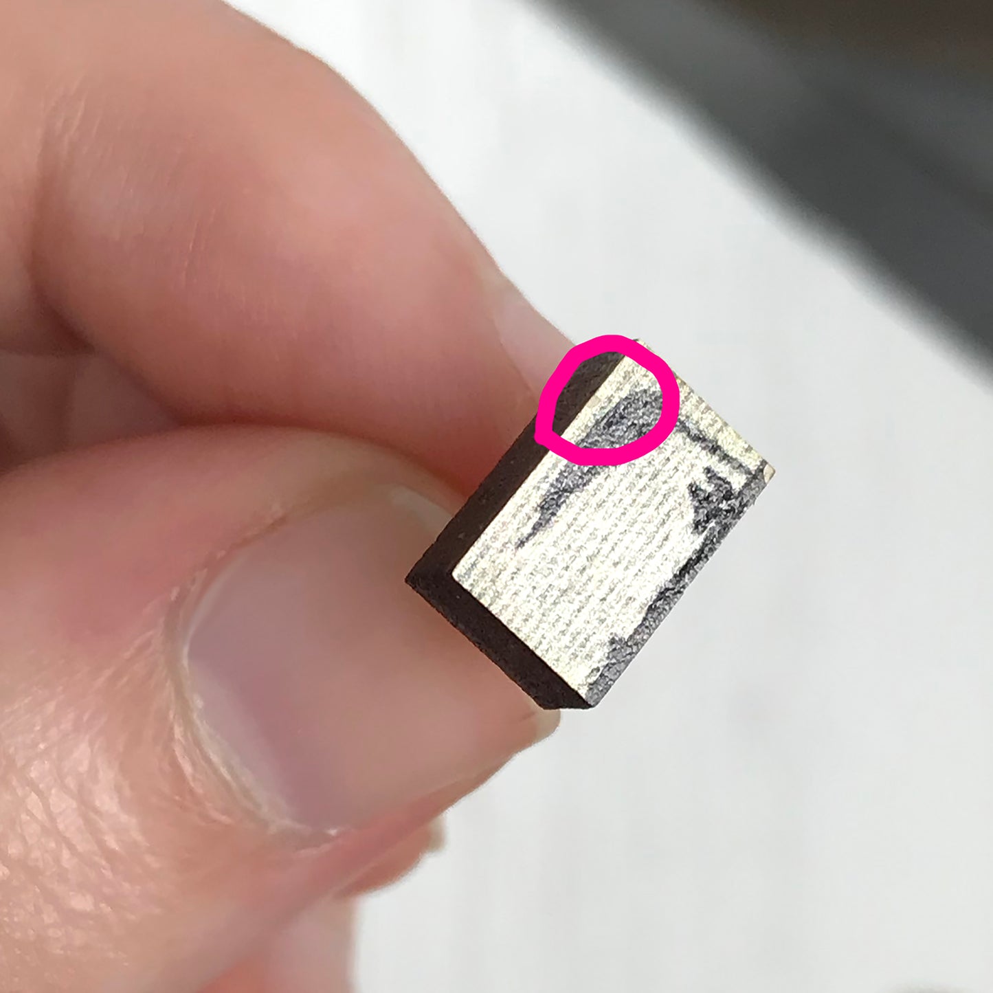 A laser cut wooden stud earring second by loadofolbobbins showing a silhouette scene inspired by the novel Wuthering Heights by Emily Brontë. The scene shows a silhouette scene of a man and woman under a windswept tree, Heathcliffe and Cathy. The scene is printed against original text from the novel. A pink circle is highlighting where a fleck of the printed image has come off.