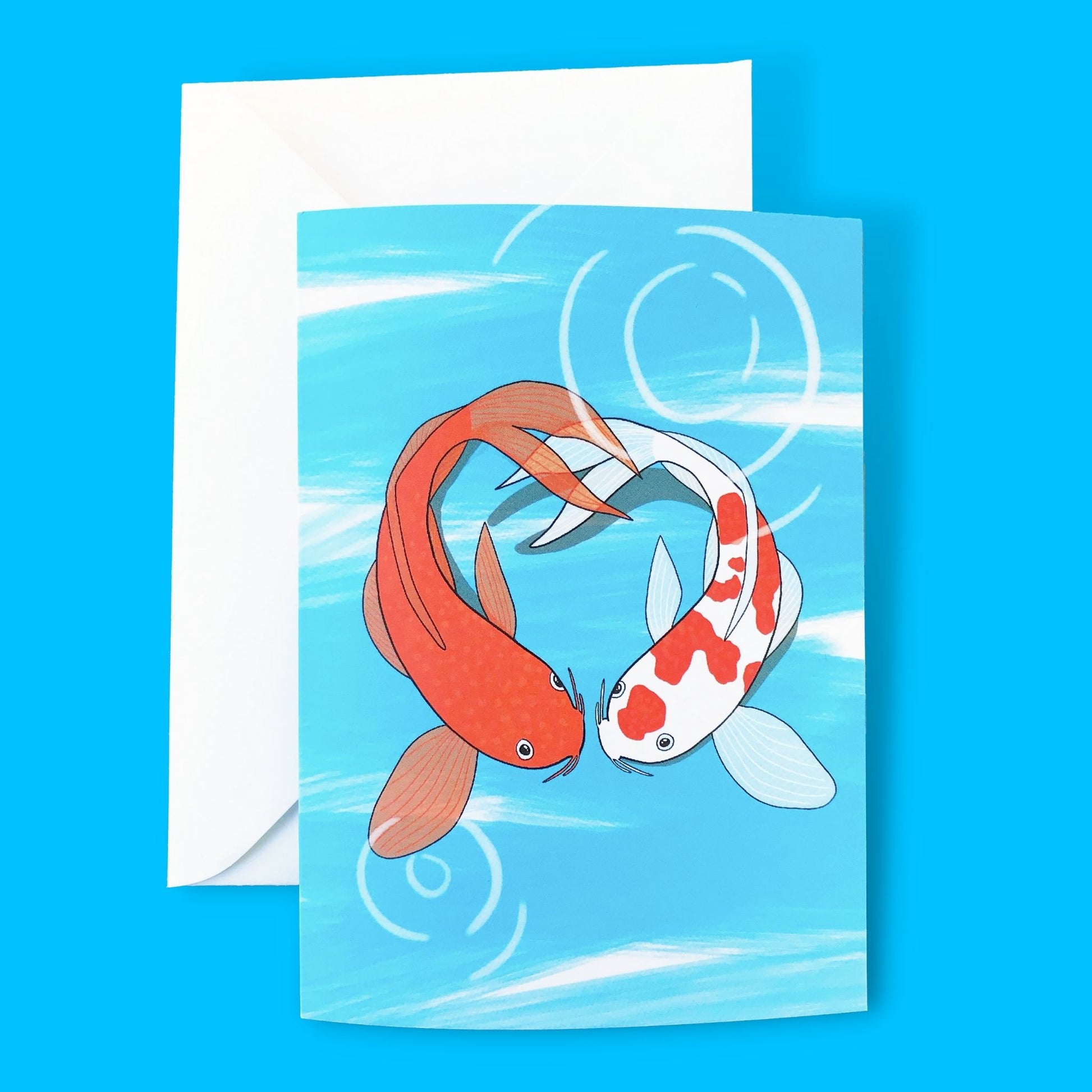 An A6 greetings card with an illustration by Loadofolbobbins of two koi fish facing each other in a pond and forming the shape of a heart. The koi on the left is a vibrant orange and the koi on the right is white with vibrant orange splodges. The background is an energetic light blue line zig zagging down the image with some white showing through. Light white circular marks show ripples on the surface of the water.