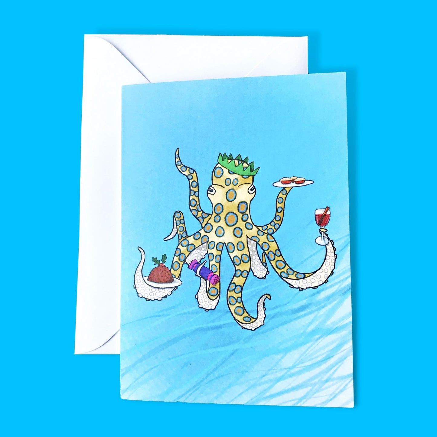 A greetings card by Loadofolbobbins. It shows a digital illustration of a Blue-ringed octopus underwater and clearly having managed to find the Christmas buffet. With a green paper crown on it's head, in four of it's tentacles it's holding festive items including a Christmas pudding, a Christmas crack, some mulled wine and a plate of mince pies.