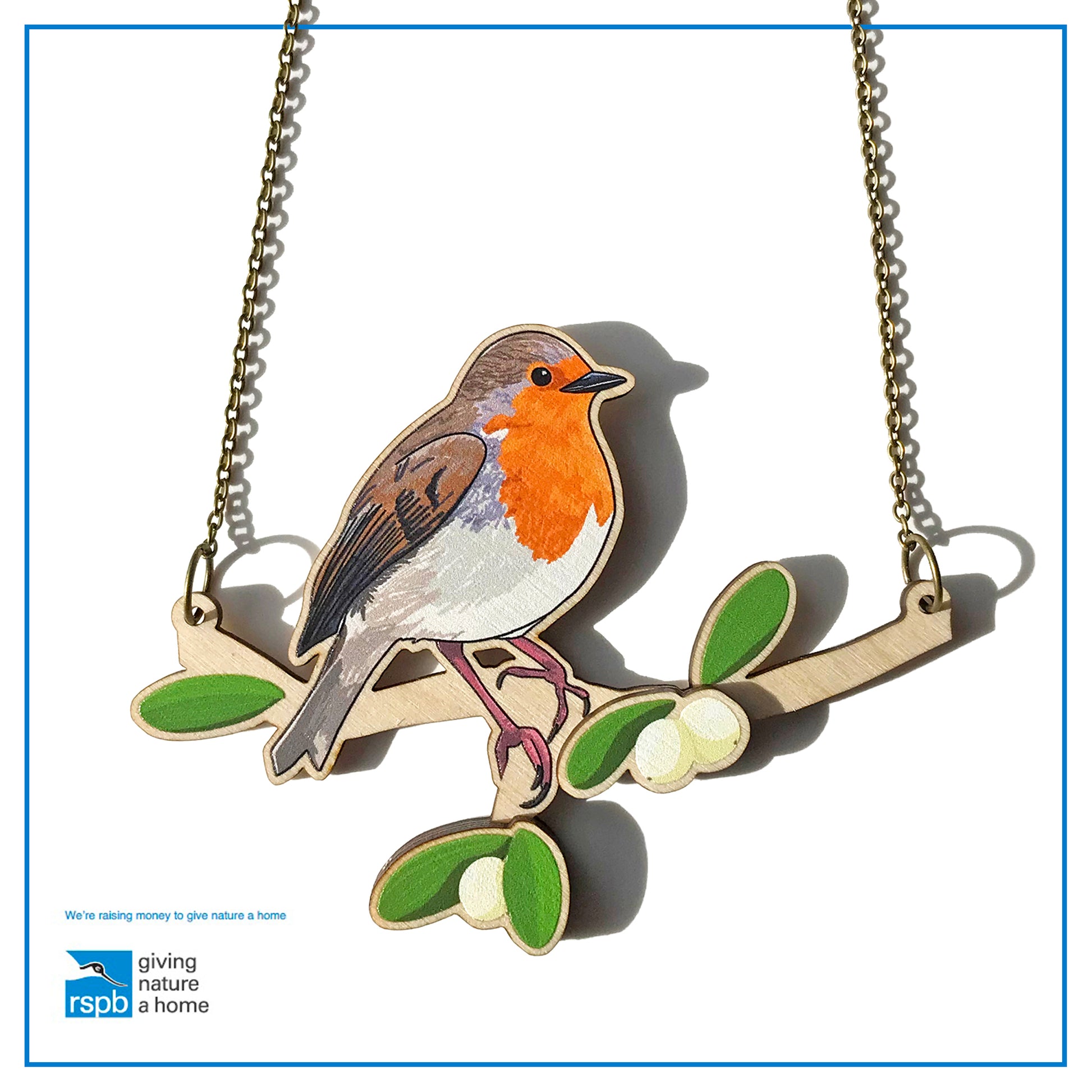 A laser cut wooden charm necklace showing an illustration of a robin bird perching on a branch with mistletoe by loadofolbobbins. The mistletoe berries and leaves stand proud of the necklace in a 3D relief effect.  The wooden necklace is hanging from an antique bronze cable chain.