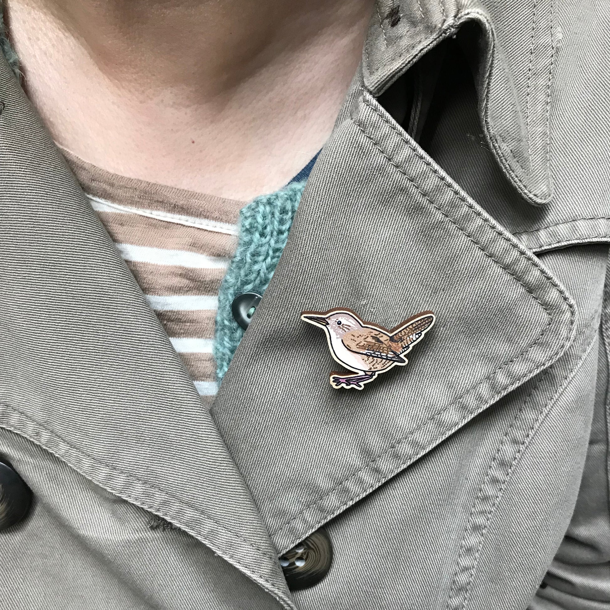 A laser cut wooden brooch showing an illustration by Loadofolbobbins of a wren. The brooch is shown on the lapel of a jacket.