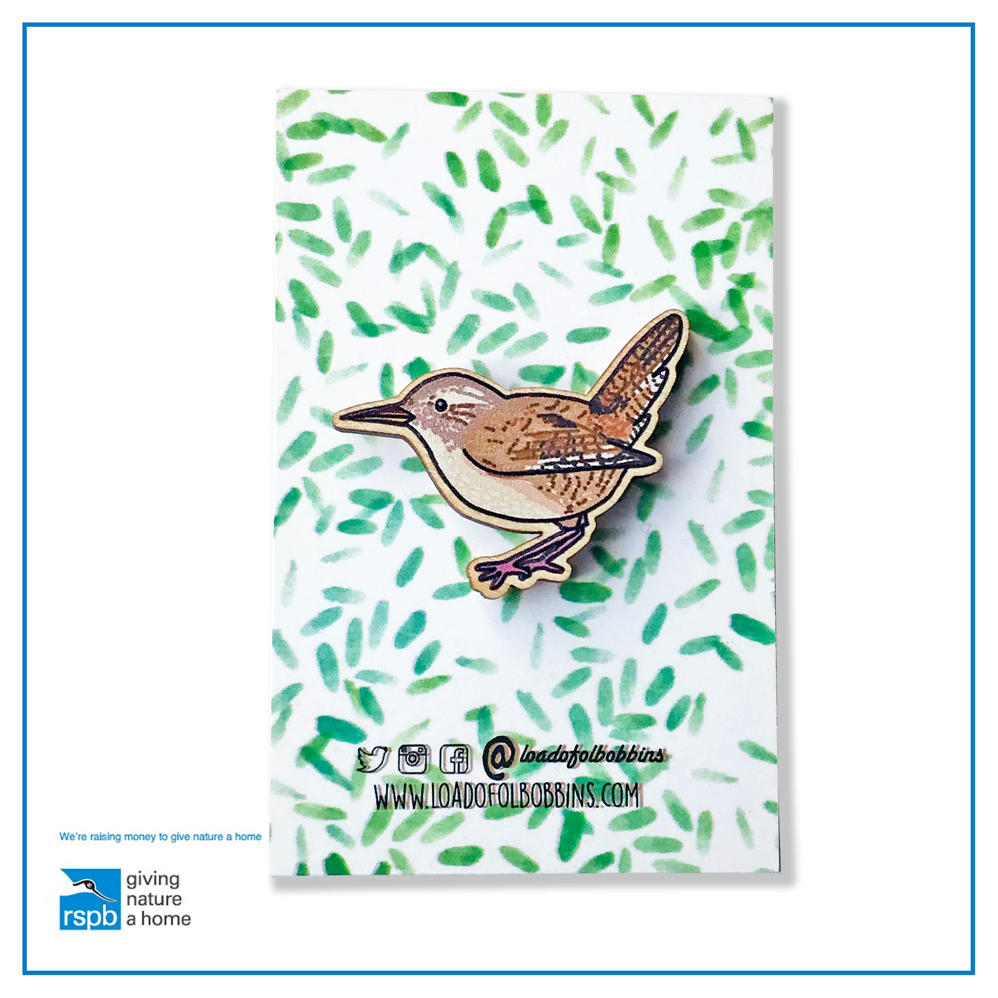 A laser cut wooden brooch showing an illustration by Loadofolbobbins of a wren. The brooch is mounted on a backing card with a repeat abstract watercolour leaf pattern.